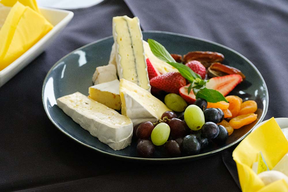 Cheese platter with strawberries, dired apricots and white and red grapes.