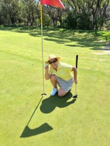 Gail Pottenger posing with a golf ball next to the hole she scored a hole in one